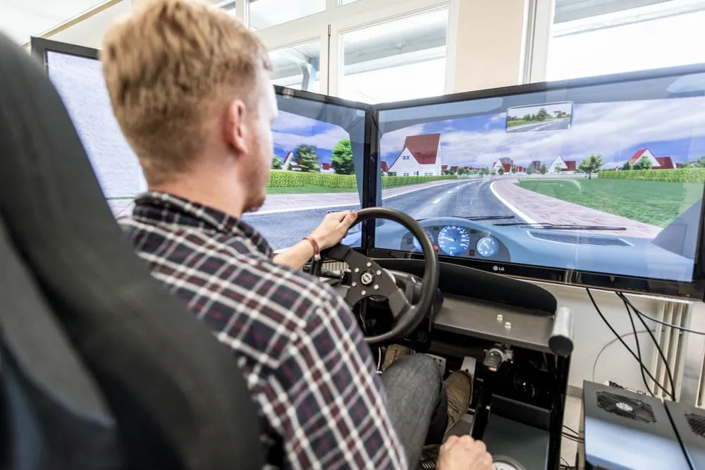 Person testet einen Fahrsimulator mit mehreren Monitoren im FH Joanneum.