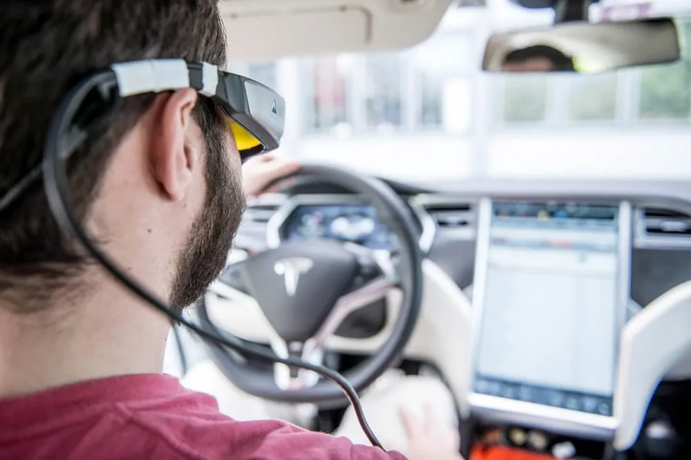 Mann sitzt mit einer VR Brille am Steuer eines Autos