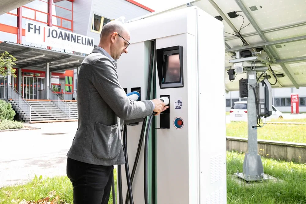 Mann lädt ein Elektrofahrzeug an einer Ladestation vor dem FH Joanneum Campus.