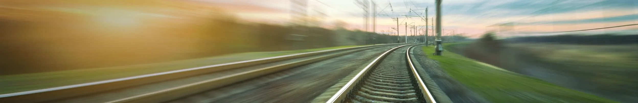 Verschwommene Zugfahrt auf einer Schienenstrecke in warmem Licht.